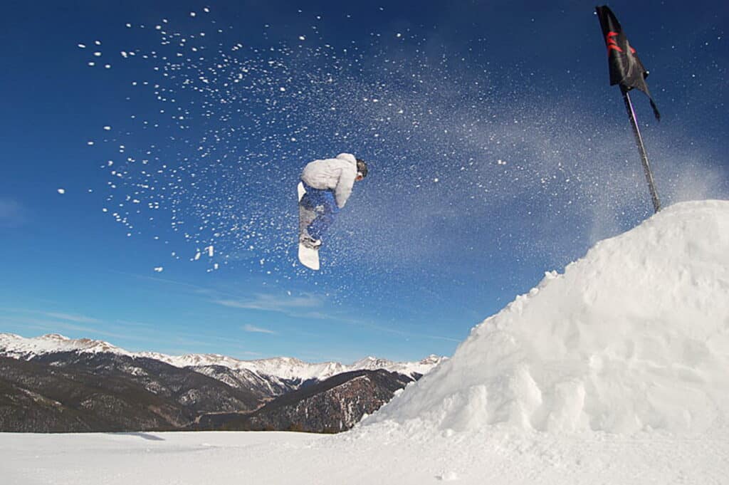 Snowboarder em pleno salto sobre uma rampa na estação de ski do Colorado, EUA, exemplificando a harmonia entre esportes de aventura e a paisagem natural.