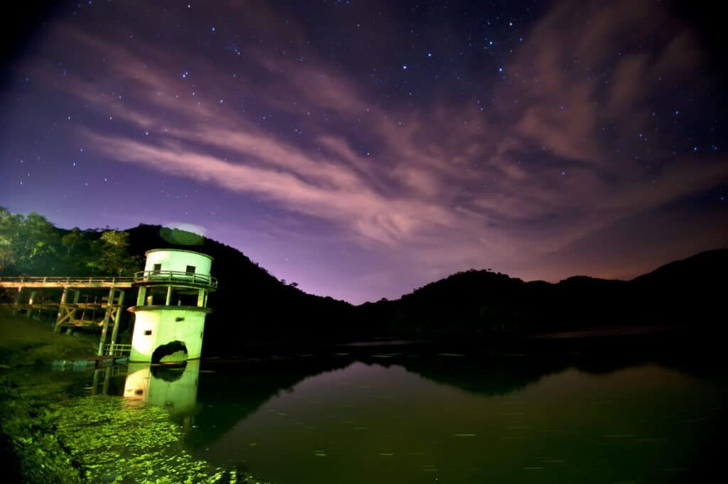 A represa da Reserva Biológica de Duas Bocas iluminada sob um céu noturno estrelado.
