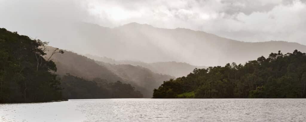 Fotografia panorâmica da Reserva Biológica de Duas Bocas ao entardecer, com raios solares permeando as nuvens sobre a represa.