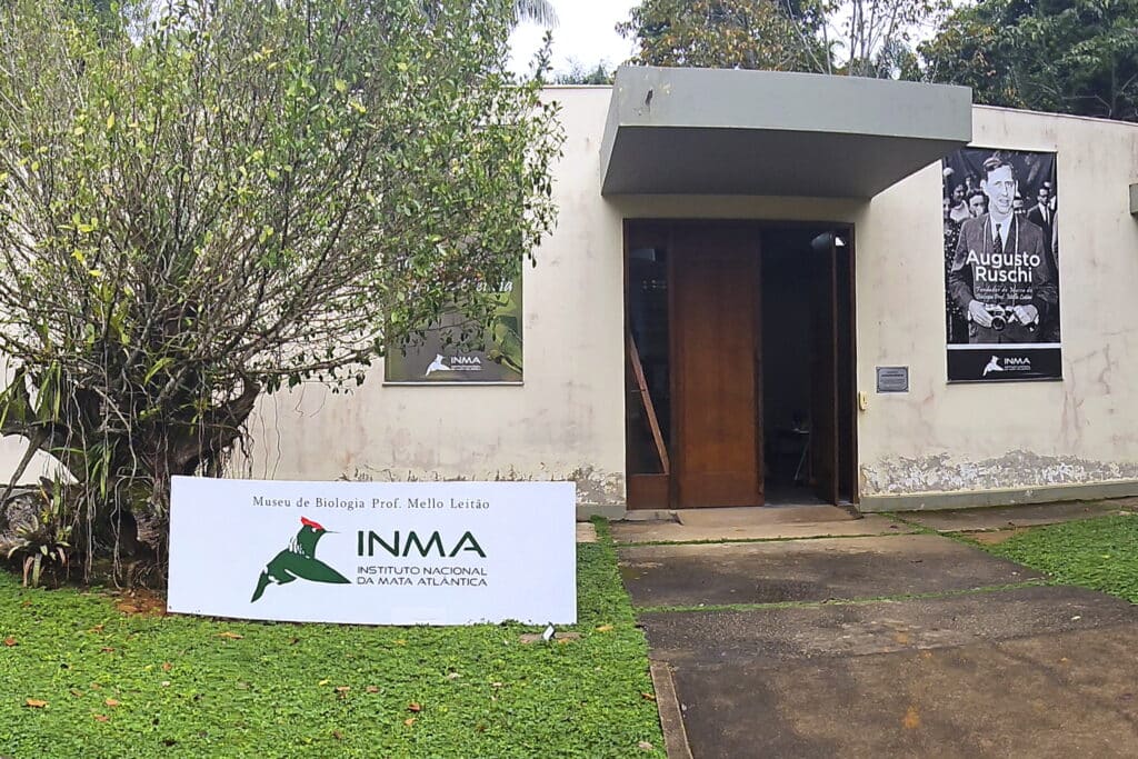 Entrada do Instituto Nacional da Mata Atlântica com placa mostrando a identidade visual que inclui a representação do beija-flor topetinho-vermelho.